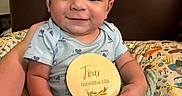 Isaac is registered to the contest to win money with this photo: animal_print, baby, blanket, blue_onesie, chair, child, cushion, cute, face, four_months_old, happy, holding, indoors, infant, person, portrait, seated, smile, wooden_sign, young