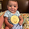 baby, infant, smile, blue_onesie, wooden_sign, four_months_old, cushion, animal_print, blanket, chair, happy, child, portrait, indoors, cute, person, seated, holding, face, young
