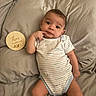 Isaac is registered to the contest to win money with this photo: baby, infant, child, onesie, bed, pillow, wooden_plaque, text, three_months_old, hand, face, eyes, curious, lying_down, clothing, skin, indoors, soft_lighting, neutral_colors, person