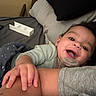 baby, infant, child, smiling, happy, face, portrait, indoors, bed, bedroom, pillow, blanket, pacifier, clothing, gray_clothing, adult_arm, hand, family, lying_down, cozy