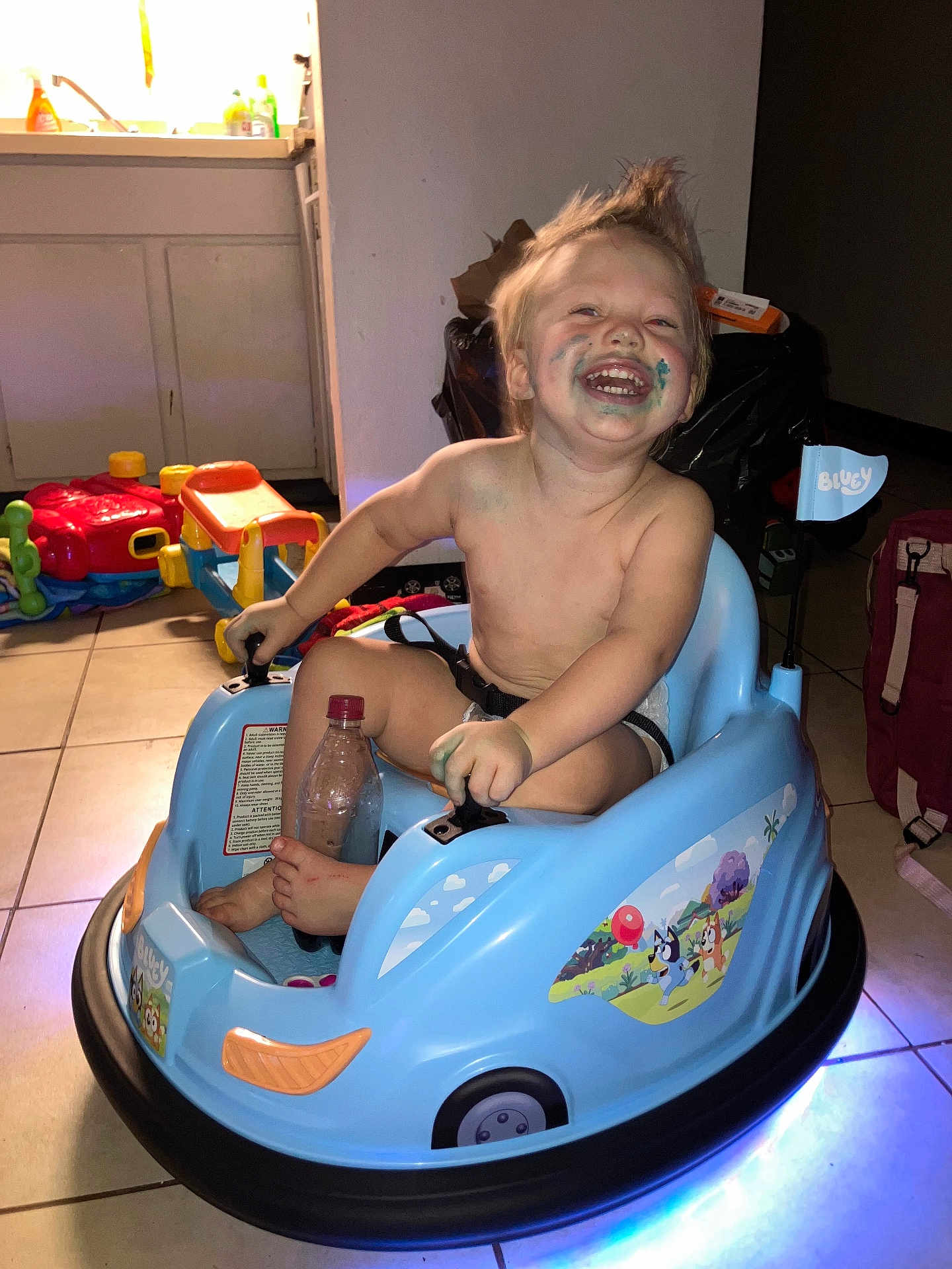 Luca joined the competition — help win amazing prizes! toddler, child, toy_car, face_paint, smiling, indoor, floor_tiles, plastic_toy, bottle, foot, happy, messy, playtime, diaper, hair_up, colorful, room, backpack, light, furniture