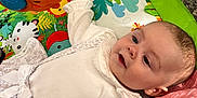 Mya is registered to the contest to win money with this photo: baby, infant, play_mat, toy, orange_toy, colorful, animal_print, white_clothing, bow, blanket, floor, rug, child, indoor, cute, portrait, laying_down, face, hand, curious