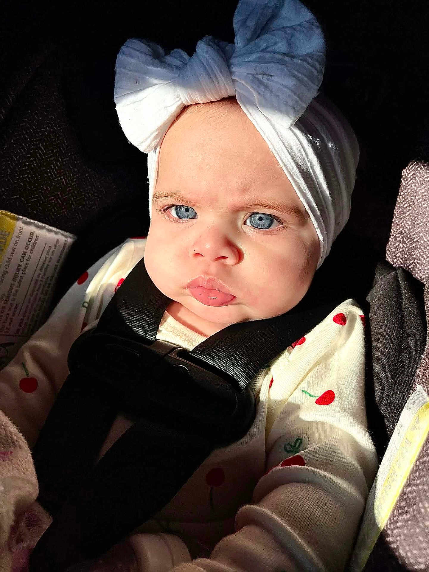 Sophia joined the competition — help win amazing prizes! baby, child, blue_eyes, white_headband, bow, car_seat, seatbelt, cherry_pattern, sunlight, infant, clothing, face, portrait, expression, young_child, cute, indoors, sitting, serious, closeup