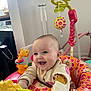 baby, smiling, child, toy, activity_center, indoor, colorful, playful, happy, infant, clothing, face, cute, fun, person, seat, pattern, bright, joyful, young