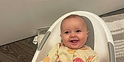 Lyla-Mae is registered to the contest to win money with this photo: baby, child, smiling, onesie, pumpkin_pattern, white_baby_seat, floor, wooden_floor, rug, hand, happy, infant, cute, indoors, portrait, sitting, clothing, face, head, person