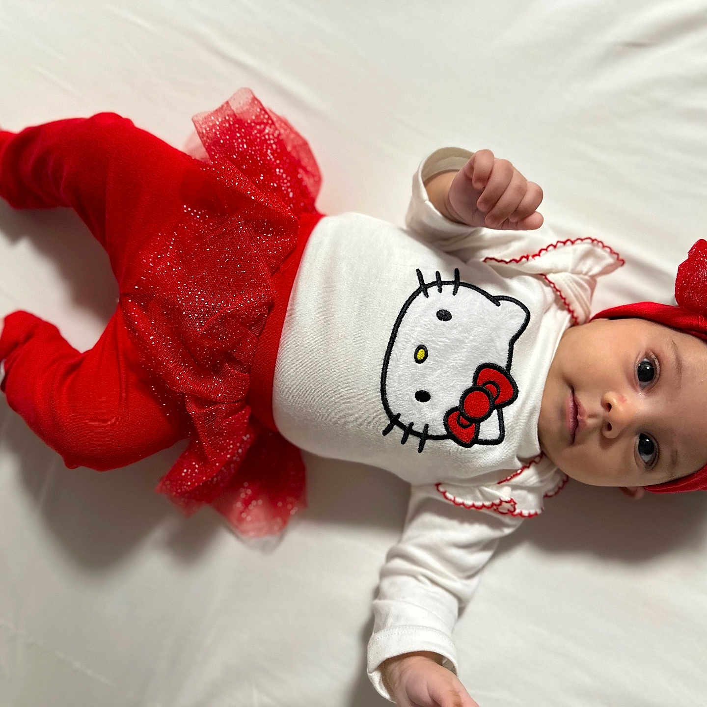 Luna Isabella joined the competition — help win amazing prizes! baby, bow, child, closeup, cute, festive, glitter, headband, hello_kitty, indoors, infant, lying_down, one_person, portrait, red_clothing, small_hands, smiling, soft_texture, toddler, white_background