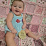 baby, child, infant, smiling, blue_clothing, flower_pattern, plush_quilt, pink, patchwork, sitting, milestone, wooden_plaque, happy, cute, portrait, indoors, person, skin, head, hand