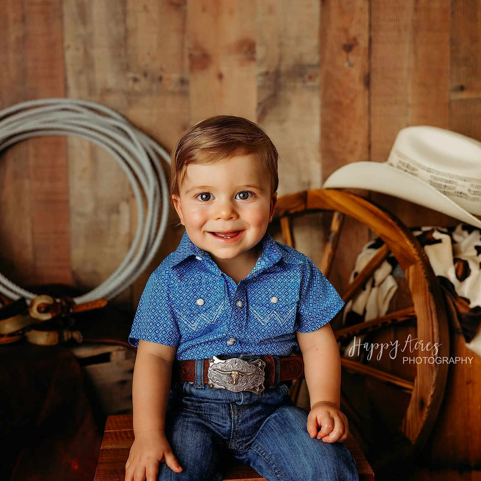 Grayson joined the competition — help win amazing prizes! belt_buckle, blue_shirt, boy, child, cowboy_hat, cowboy_outfit, cowhide_blanket, happy, indoor, jeans, photography, portrait, rope, rustic, sitting, smiling, toddler, wagon_wheel, western_theme, wooden_background