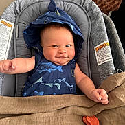 Demetrius is registered to the contest to win money with this photo: baby, infant, hood, blue_clothing, shark_pattern, smile, face, arm, blanket, pacifier, baby_seat, cushion, indoor, child, cute, happy, person, skin, head, expression