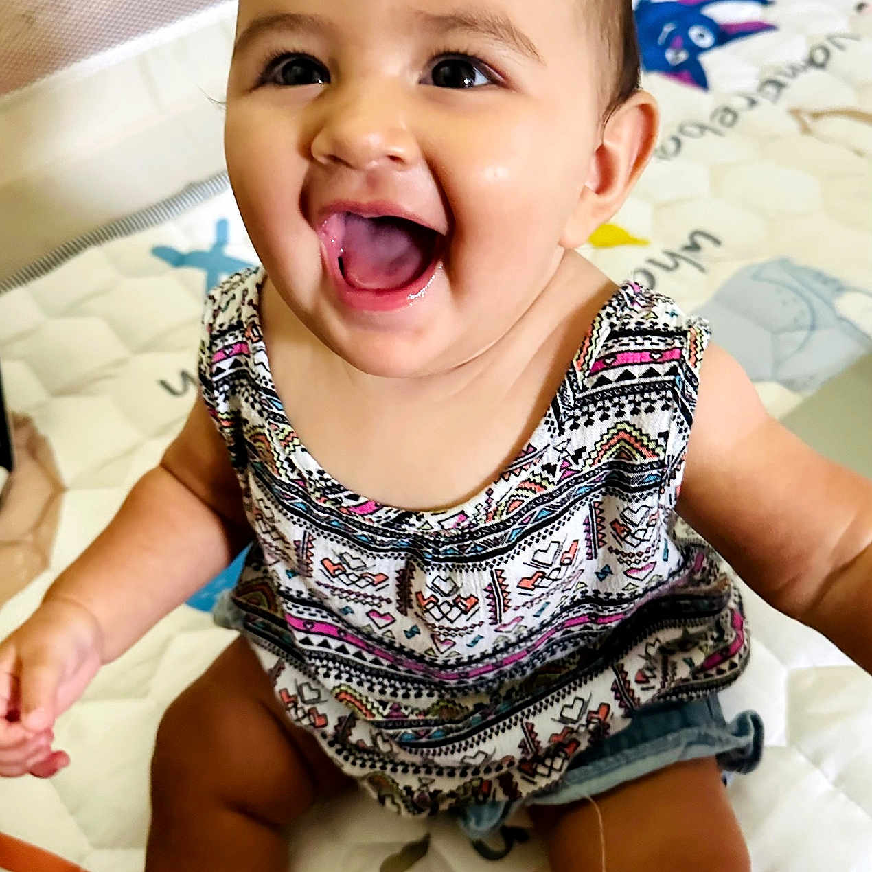 Shiloh William is registered to the contest to win money with this photo: baby, child, smiling, happy, sitting, play_mat, indoor, clothing, patterned_top, denim_shorts, face, cute, portrait, infant, skin, eyes, mouth, cheerful, young, person