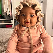 Maena participe au concours pour gagner de l'argent avec cette photo : baby, child, infant, knit_bonnet, pink_outfit, smiling, face, indoor, lamp, wardrobe, clothing, furniture, portrait, cute, seated, soft_lighting, cozy, home, person, young_child