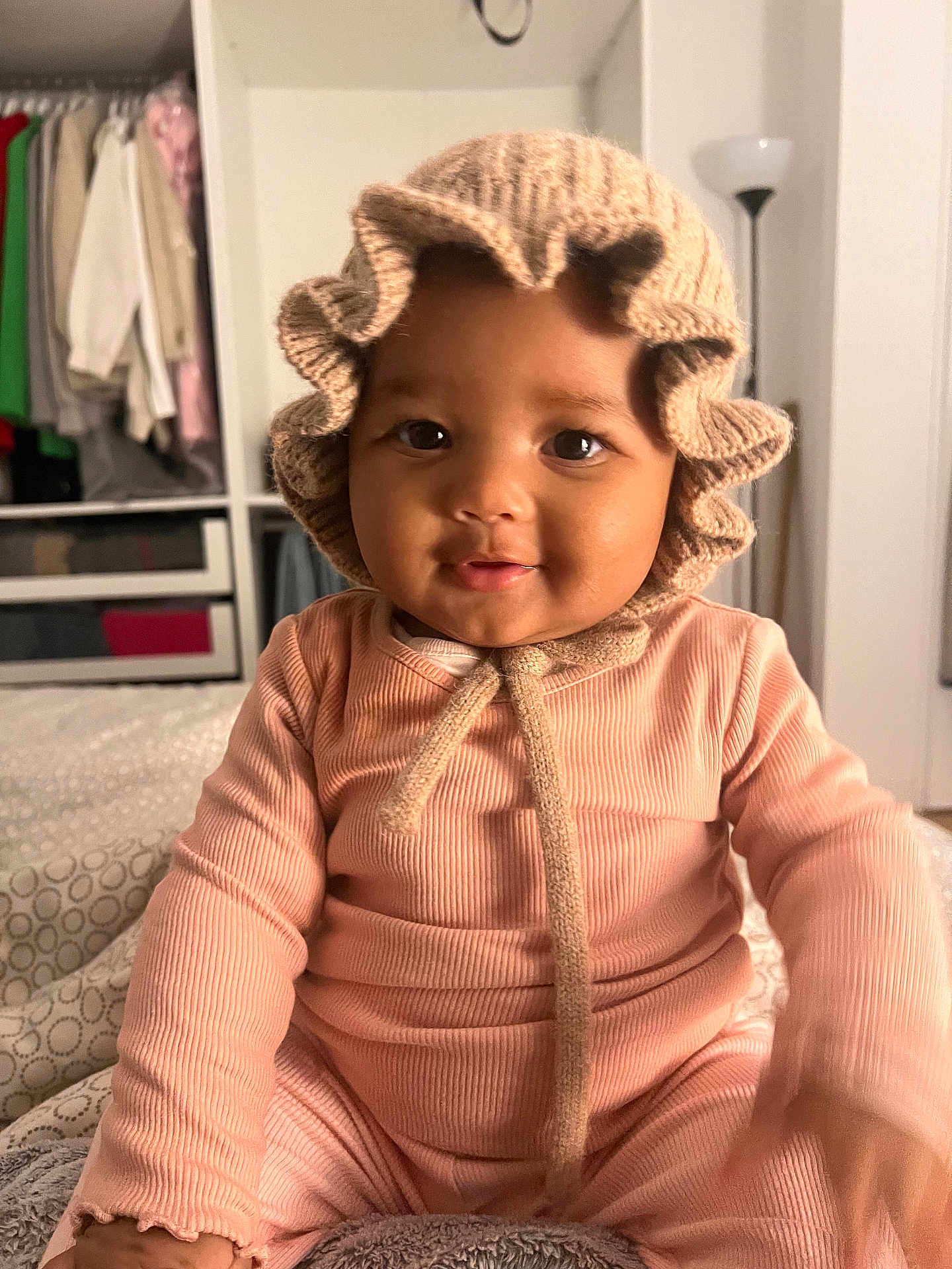 Maena participe au concours pour gagner de l'argent avec cette photo : baby, child, infant, knit_bonnet, pink_outfit, smiling, face, indoor, lamp, wardrobe, clothing, furniture, portrait, cute, seated, soft_lighting, cozy, home, person, young_child