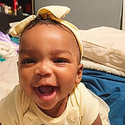 Isabella is registered to the contest to win money with this photo: baby, smiling, happy, infant, headband, yellow_clothing, tulle_skirt, bed, blanket, indoor, portrait, cute, child, toddler, closeup, person, skin, face, apparel, joy