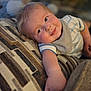 baby, child, smiling, couch, patterned_fabric, indoor, portrait, cute, arm, blond_hair, striped_shirt, bib, relaxed, infant, closeup, soft_light, happy, person, home, cozy