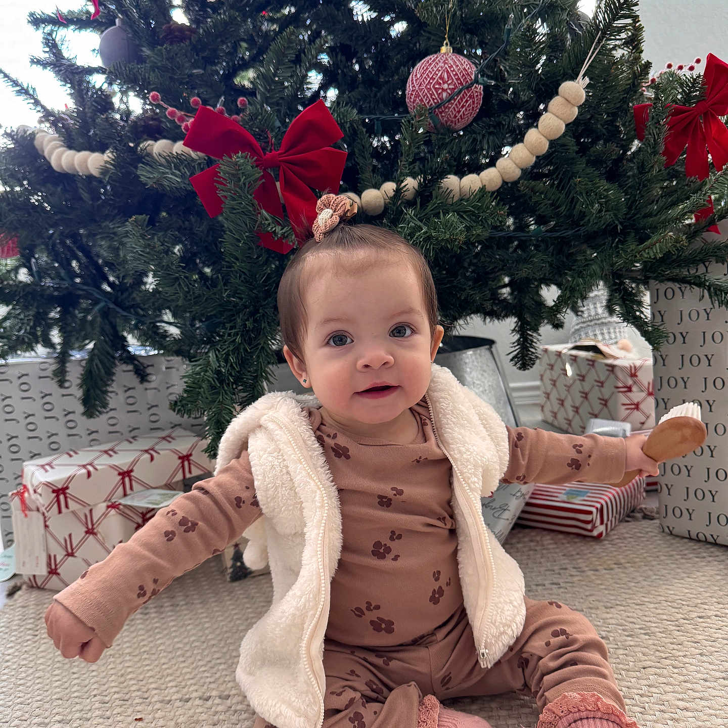 Maríaelisa is registered to the contest to win money with this photo: baby, carpet, child, christmas_tree, cute, decorations, festive, gift_wrap, holiday, holiday_season, home, indoor, pajamas, presents, red_bow, sitting, smiling, socks, toy, vest