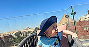 Adham joined the competition — help win amazing prizes! baby, child, hat, blue_clothing, outdoor, chair, cushion, sunny, sky, pyramids, glasses, building, railing, footwear, shorts, smiling, person, portrait, daylight, balcony