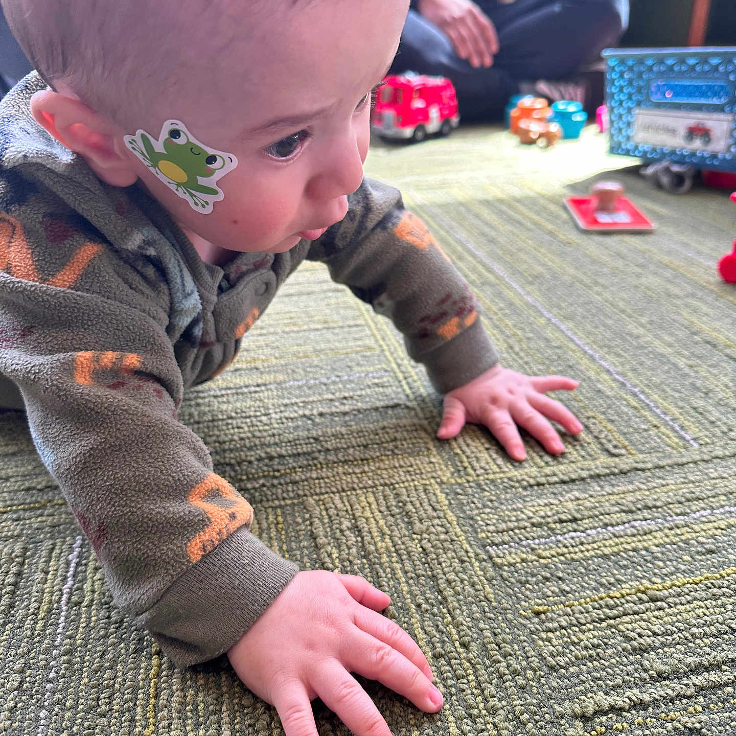 Adham joined the competition — help win amazing prizes! baby, child, crawling, frog_sticker, carpet, toy, indoor, focus, hand, face, person, floor, clothing, young_child, curious, background, adult, sitting, colorful, play