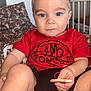 child, toddler, baby, kid, face, eyes, blue_eyes, blond_hair, hair, red_shirt, shirt, cookie, snack, crib, bedding, pillow, blanket, sitting, portrait, indoor
