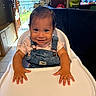 baby, bow, child, daylight, denim_overalls, doorway, face, floral_shirt, furniture, hands, happy, high_chair, home, indoor, portrait, sitting, smiling, television, tray, window