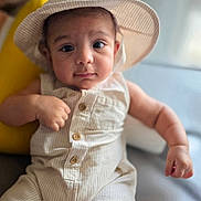 Omar is registered to the contest to win money with this photo: baby, infant, hat, romper, clothing, face, eyes, skin, hand, cute, portrait, indoors, soft_light, expression, child, young, sitting, button, headwear, person