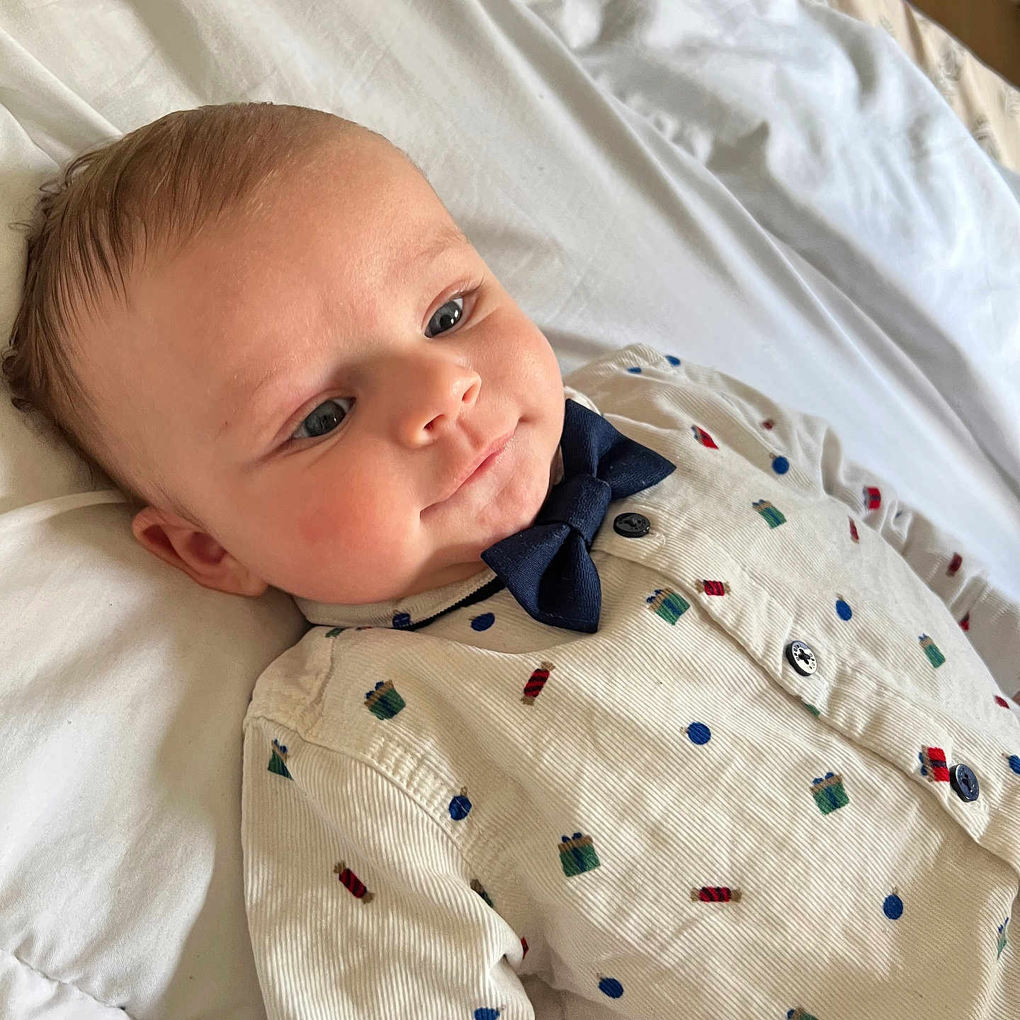 Cassim participe au concours pour gagner de l'argent avec cette photo : adorable, baby, bed, blue_eyes, bow_tie, cheek, closeup, cozy, happy, infant, infant_fashion, lying_down, newborn, onesie, patterned_clothing, pillow, portrait, rosy_cheeks, sheet, soft_light