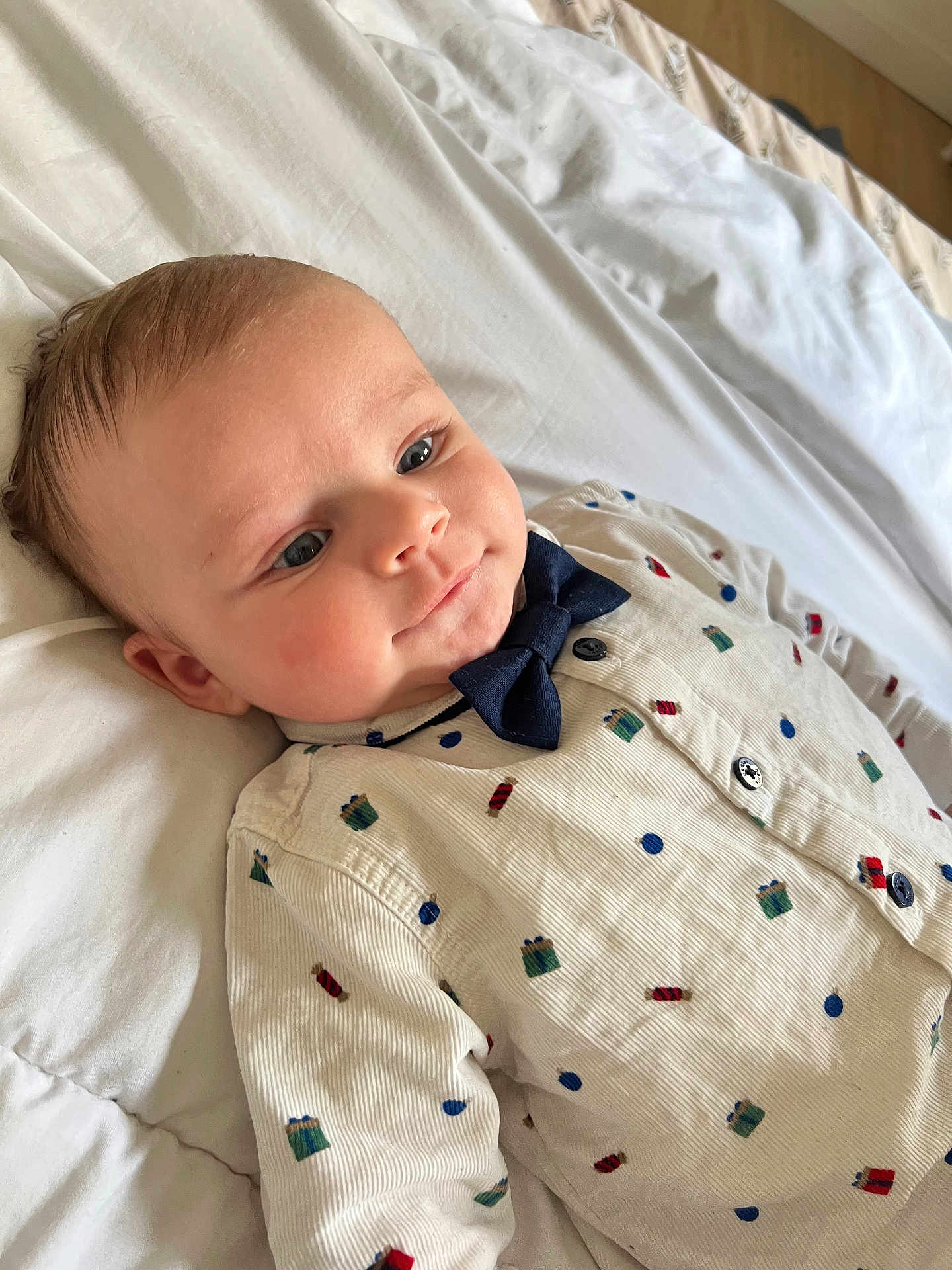 Cassim participe au concours pour gagner de l'argent avec cette photo : baby, infant, newborn, bow_tie, onesie, patterned_clothing, blue_eyes, rosy_cheeks, cheek, lying_down, bed, pillow, sheet, closeup, portrait, soft_light, cozy, happy, adorable, infant_fashion