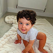 Malikai joined the competition — help win amazing prizes! toddler, child, baby, curly_hair, blue_eyes, crawling, blanket, carpet, indoors, smiling, cute, happy, person, skin, foot, hand, head, room, radiator, clothing
