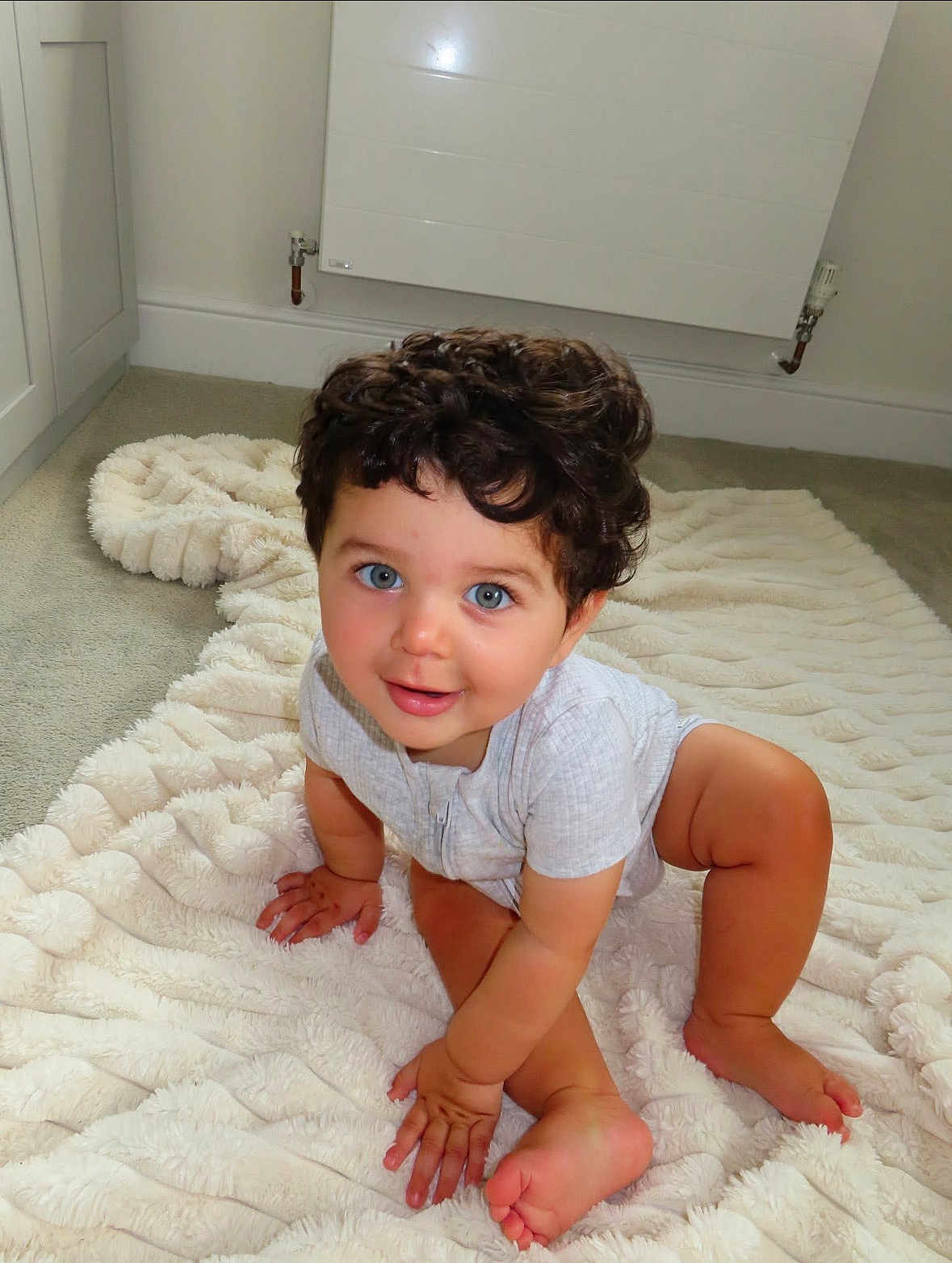 Malikai joined the competition — help win amazing prizes! toddler, child, baby, curly_hair, blue_eyes, crawling, blanket, carpet, indoors, smiling, cute, happy, person, skin, foot, hand, head, room, radiator, clothing