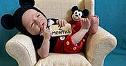 Wyatt joined the competition — help win amazing prizes! baby, infant, mickey_mouse, costume, armchair, plush_toy, sign, blue_background, cute, red_clothing, black_clothing, smiling, small_chair, soft_rug, child, portrait, sitting, indoor, newborn, toy