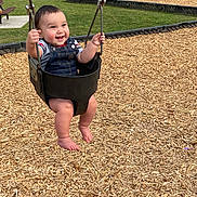 Barric is registered to the contest to win money with this photo: baby, child, swing, playground, park, grass, wood_chips, smile, happy, overalls, denim, barefoot, outdoor, daylight, picnic_table, swing_set, person, infant, joyful, fun