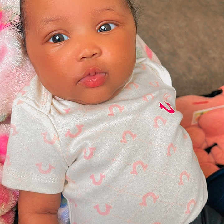 Miangel joined the competition — help win amazing prizes! baby, infant, pink_bow, white_shirt, patterned_clothing, curly_hair, indoors, blanket, cute, child, portrait, closeup, skin, face, lying_down, expression, cozy, soft_toys, floor, casual