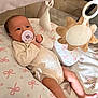 baby, infant, pacifier, play_mat, soft_toy, sun_toy, cushion, pink_bows, clothing, legs, feet, face, hand, indoor, child, cute, relaxed, newborn, comfort, toy