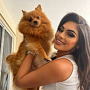 Coco Chanel joined the competition — help win amazing prizes! woman, dog, pom, fluffy, smiling, portrait, indoor, pet, holding, long_hair, makeup, watch, white_top, cute, friendly, face, eyes, furniture, window, natural_light
