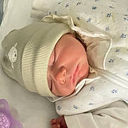 Lena participe au concours pour gagner de l'argent avec cette photo : newborn, baby, sleeping, hat, pacifier, hospital_bed, blanket, white_clothing, infant, cute, peaceful, child, face, hand, soft, resting, indoors, portrait, cozy, sleep