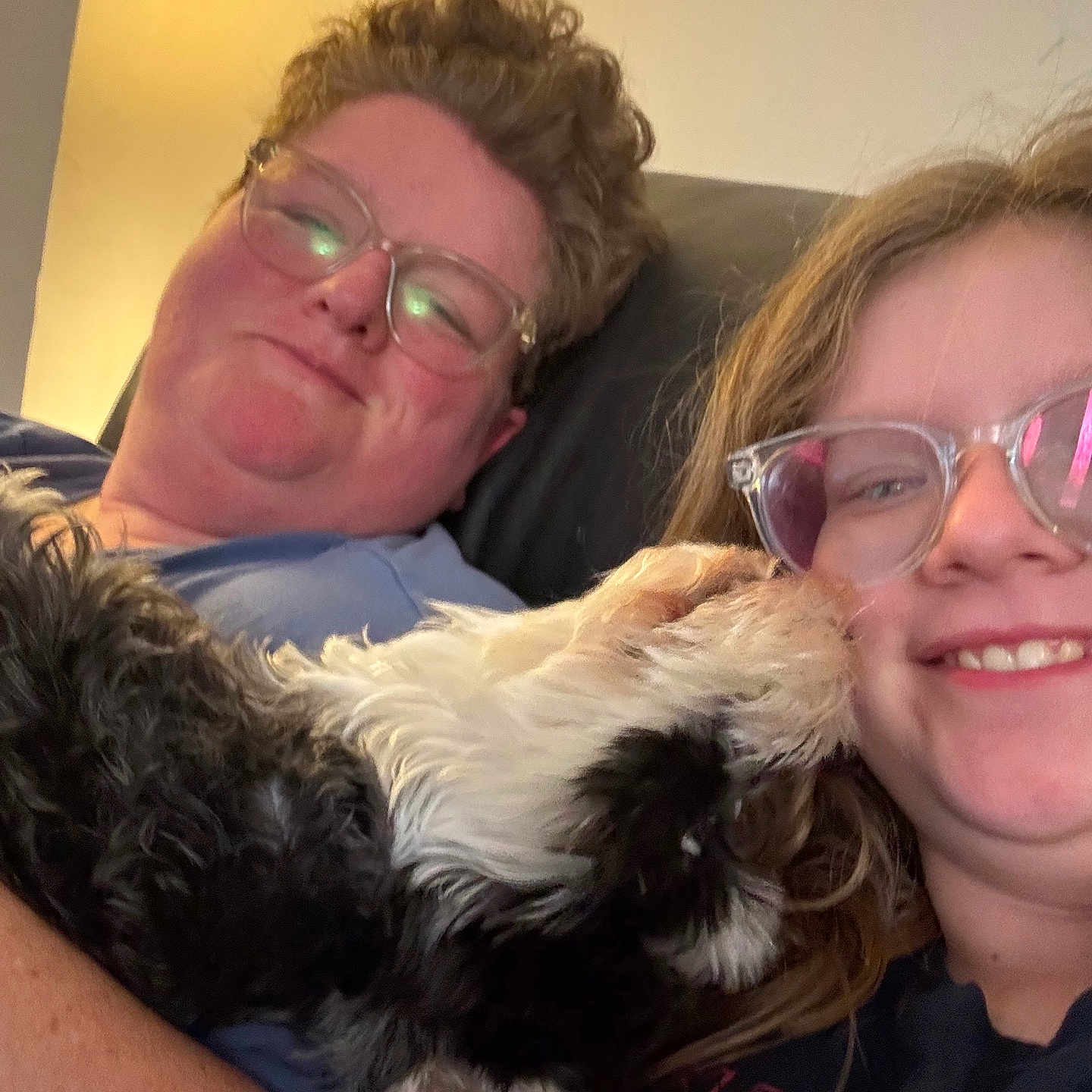 Minnie joined the competition — help win amazing prizes! person, glasses, smiling, dog, licking, cuddle, indoor, warm_lighting, hair, face, happy, casual_clothing, black_and_white_dog, close_up, seated, pet, love, affection, eyewear, relaxation