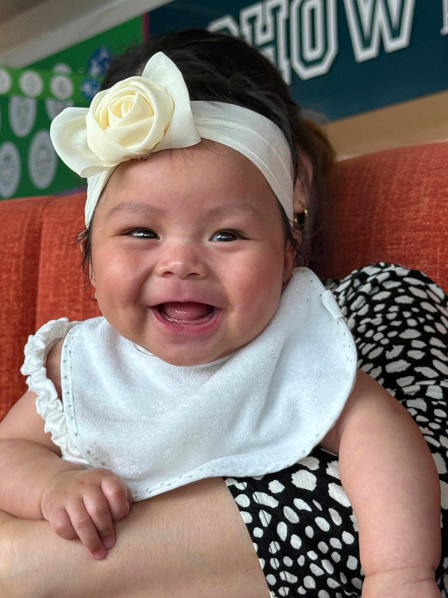 Lauren is registered to the contest to win money with this photo: baby, smile, headband, flower, bib, arm, person, clothing, couch, orange, polka_dot, black_and_white, happy, indoor, holding, face, skin, child, background, portrait