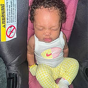 Jhournie is registered to the contest to win money with this photo: baby, infant, sleeping, curly_hair, white_tank_top, yellow_pants, car_seat, warning_label, child, cute, peaceful, indoors, clothing, sock, seat, safety, person, portrait, resting, young