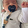 baby, sleeping, pacifier, white_shirt, beaded_pacifier_clip, crocodile_logo, infant, cute, child, newborn, hand, face, closed_eyes, lying_down, bed, blanket, clothing, blue, wooden_beads, cute_accessory