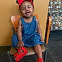 Dior is registered to the contest to win money with this photo: carpet, chair, child, cute, denim_dress, fashion, floor, footwear, furniture, hair, happy, indoor, person, portrait, red_bow, red_sandals, sitting, smiling, toddler, young