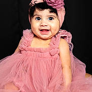 Leia is registered to the contest to win money with this photo: baby, child, infant, pink_dress, headband, flower, smiling, sitting, curly_hair, cute, portrait, happy, studio, tulle, fashion, adorable, closeup, face, young_child, dark_background