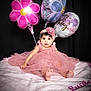 baby, child, pink_dress, headband, balloons, flower_balloon, birthday, blanket, curly_hair, portrait, celebration, cute, smiling, soft_texture, sitting, indoor, happy, young_child, person, festive