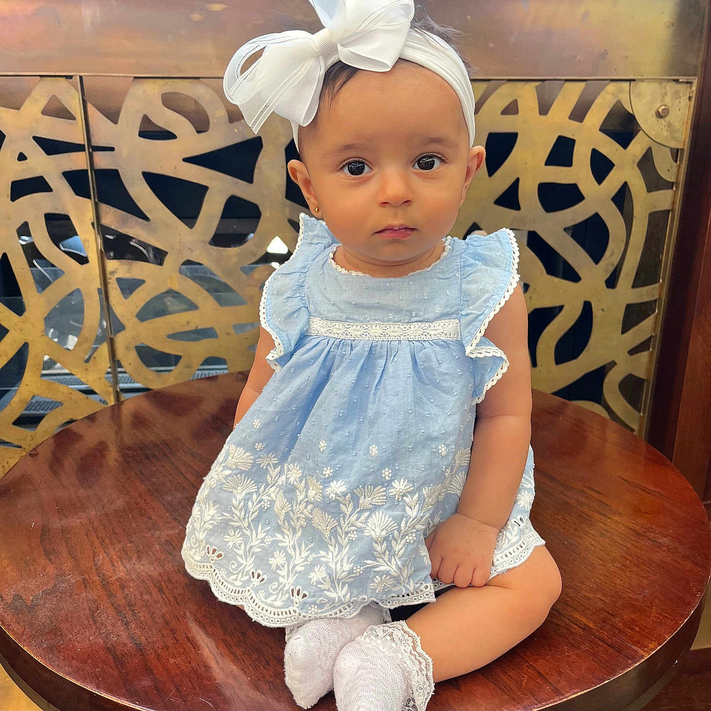 Mahratie is registered to the contest to win money with this photo: accessory, baby, blue_dress, bow, child, closeup, cute, decorative_background, expression, eye_contact, face, fashion, girl, headband, indoors, portrait, sitting, white_socks, wooden_table, young_child