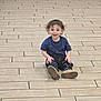 Michael joined the competition — help win amazing prizes! child, toddler, sitting, indoor, tiled_floor, smile, happy, blue_shirt, jeans, boots, curly_hair, face, portrait, center_composition, brick_wall, floor_vent, playful, single_person, brown_shoes, casual_clothing