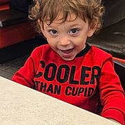 Michael joined the competition — help win amazing prizes! child, toddler, smile, happy, red_shirt, text_on_clothing, curly_hair, portrait, indoor, restaurant, table, booth_seating, eyes, playful, cute, dining, casual_clothing, person, expressive_face, young_child