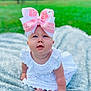 Emmy is registered to the contest to win money with this photo: baby, child, infant, bow, white_dress, blanket, outdoor, grass, greenery, cute, portrait, sitting, curious, face, headwear, soft_light, daylight, candid, skin, hands
