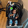 baby, child, car_seat, denim_overalls, headband, toy, indoor, wooden_floor, chair, cabinet, flooring, baby_clothes, seat_belt, infant, cute, child_seat, room, baby_toy, sitting, calm