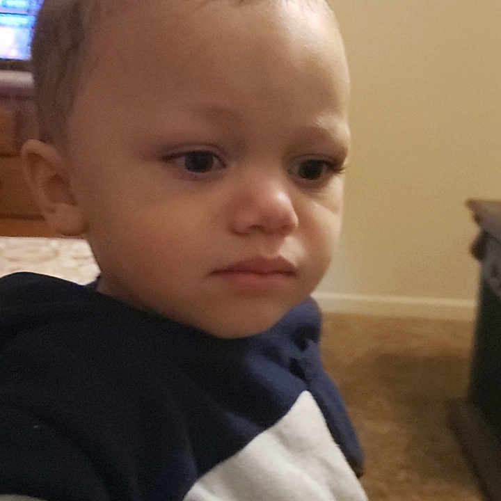 Stetson is registered to the contest to win money with this photo: brown_hair, carpet, casual_clothing, child, closeup, curly_hair, curly_topknot, expression, face, furniture, home, hoodie, indoor, person, portrait, serious, skin, toddler, young, young_child