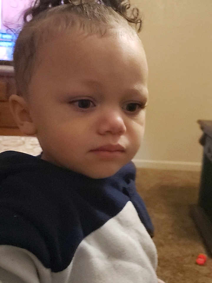 Stetson is registered to the contest to win money with this photo: toddler, child, indoor, curly_hair, hoodie, person, face, expression, young, carpet, furniture, brown_hair, closeup, portrait, casual_clothing, home, young_child, serious, curly_topknot, skin