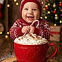 baby, child, smiling, red_hat, knitwear, candy_cane, whipped_cream, hot_chocolate, christmas_tree, holiday_lights, gingerbread_cookie, peppermint, wooden_platter, powdered_sugar, festive, winter_clothing, indoor, portrait, cozy, cute