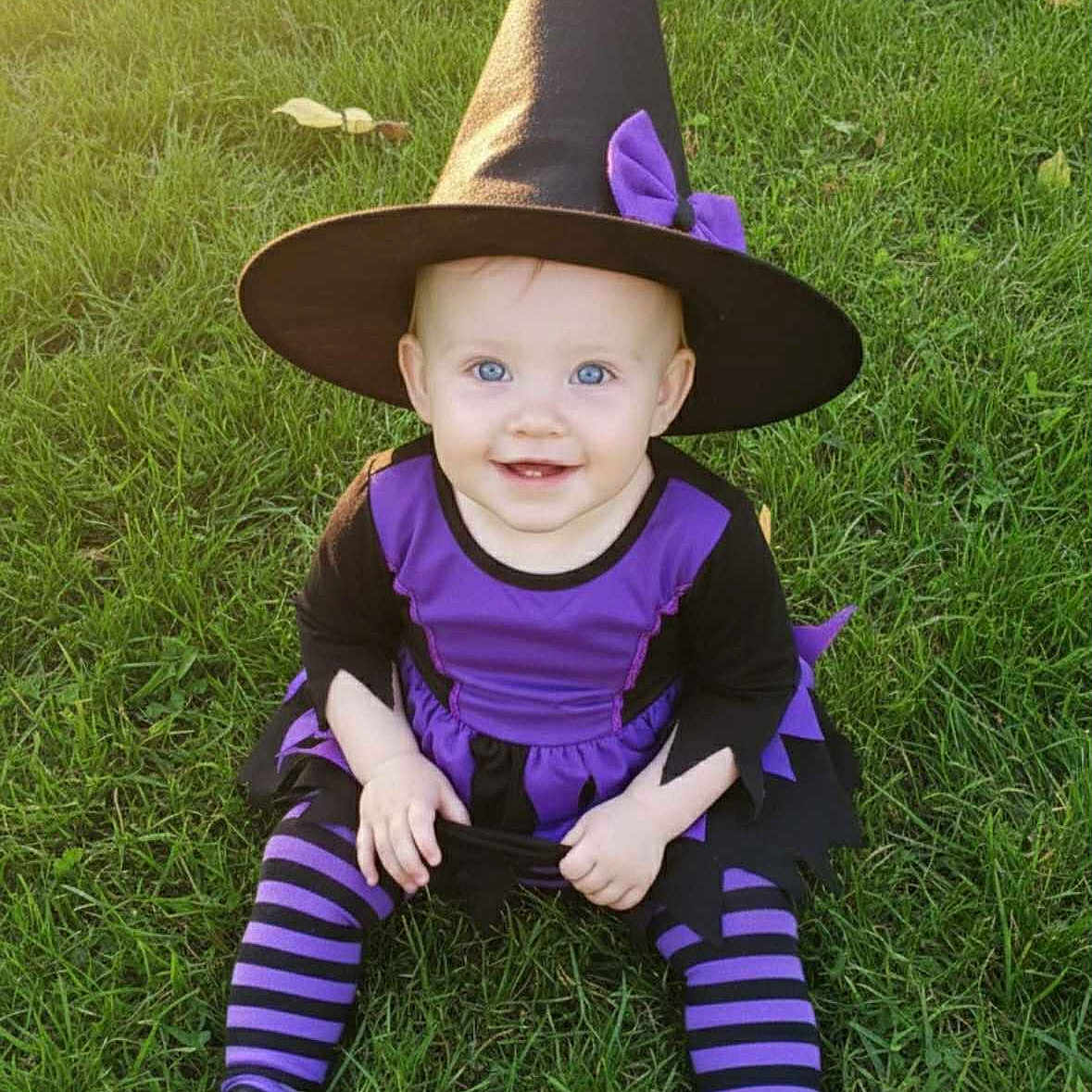 Miranda joined the competition — help win amazing prizes! baby, black, blue_eyes, child, costume, cute, festive, grass, happy, hat, holiday, outdoor, playful, portrait, purple, sitting, smile, striped_tights, sunlight, witch_costume